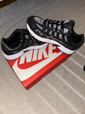 Nike p6000 - Säljer ett par helt nya snygga Nike sneakers i svart och grått med vit sula. Skorna har mesh- och syntetpaneler, klassisk snörning och diskret Swoosh-logga på sidan. Perfekta för dig som gillar sportig och modern stil. Storlek 42, passar även 41-43