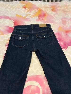  nya oandvända Lager 157 mörkblå jeans - Mörkblå lager 157 jeans med klassisk bootcut passform. Jeansen har fem fickor, silverfärgade knappar och kontrastsömmar. Tillverkade i slitstarkt denimtyg som ger en tidlös look. Perfekta för dig som gillar retrovibbar och vill ha ett par jeans som sticker ut.