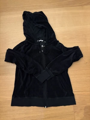 Svart velour hoodie från Cubus, stl M - Mjuk och skön svart hoodie i velour från Cubus, storlek M. Tröjan har huva med snörning, dragkedja framtill och två fickor. Perfekt för chill dagar och har en loose passform med långa ärmar och ribbade muddar. Säljer även matchande mjukisbyxor till. 80% Bomull, 20% Polyester