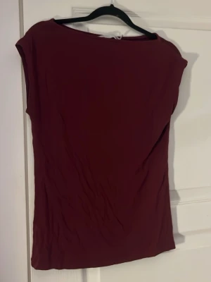 Vinröd tight t-shirt i bomull - Säljer en vinröd t-shirt med tight passform. T-shirten är enkel och stilren utan mönster, har korta ärmar och är gjord i mjuk bomull. Perfekt att matcha med jeans eller kjol för en clean look.