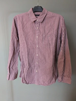 Rutig skjorta från Skill  - Rutig skjorta från Skill i storlek L. Skjortan har ett klassiskt rödvitt rutmönster, lång ärm och knäppning framtill. Bröstficka med sned rutdetalj och mjukt bomullsmaterial. Perfekt för dig som gillar en avslappnad men ändå stilren look.