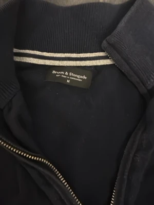 Bruun & Stengade Full-zip Cardigan – Strl M fast passar som S  - Kan tänka mig gå ner i pris. Säljer en klassisk mörkblå full-zip cardigan från kvalitetsmärket Bruun & Stengade. En perfekt baströja som passar till det mesta. Tröjan är i ett skönt material och har en stilren passform Skick: Tröjan är använd och har blivit något urtvättad i färgen, vilket ger den en lite mer avslappnad look Notera: Dragkedjan har blivit lite "vågig/fladrig" när man bär tröjan öppen (se bild), men den fungerar felfritt och ser bra ut när den är stängd. 