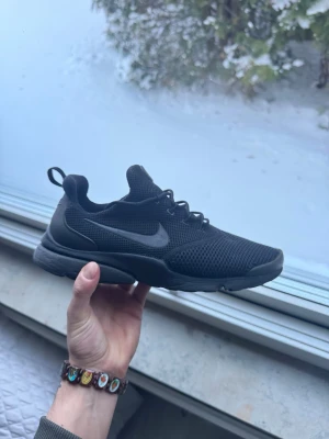 Nike Presto fly sneakers - Säljer ett par helsvarta Nike Presto sneakers med mesh-överdel och snyggt ton-i-ton swoosh på sidan. Skorna har snörning, platt sula och rund tå. Perfekta för dig som gillar stilrena och sportiga sneakers med skön passform.