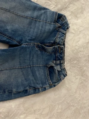 W34cm, inneben:78cm, total längd:100cm - Säljer ett par blå jeans från Lindex i modellen Freja. Jeansen har bootcut-ben, klassisk femficksdesign och stängs med dragkedja och knapp. Materialet är jeans i bomull och de har snygga slitningar för en cool look. Perfekta för dig som gillar en avslappnad stil.