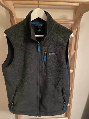 Patagonia fleece väst - En patagonia väst i fleece material i bra skick. Västen är svart med blåa detaljer så den sticker ut och blir mer unik. Inga defekter och lite använd. Annars är den i ny skick. Den är perfekt för hösten som kommer eller för vinter som mellanlager. Väster är väldigt varm och bekväm med bra passform för storlek M. Kom med bud. Jag skickar samma dag.