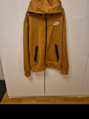 Nike mjukisbyxor i senapsgult - Snygga mjukisbyxor från Nike i en senapsgul färg med svarta dragkedjor vid fickorna och vit Nike-logga på benet. Byxorna har ribbade muddar vid benslut och snörning i midjan för extra komfort. Perfekt för chill eller träning.