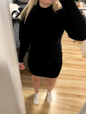 Svart stickad kortklänning - Säljer en svart stickad kortklänning med lång ärm och hög hals. Klänningen har en tight passform och är perfekt för dig som gillar en enkel men stilren look. Supermjuk och skön att ha på sig, passar till många olika tillfällen. Köpt på Nelly från NellybyNelly 