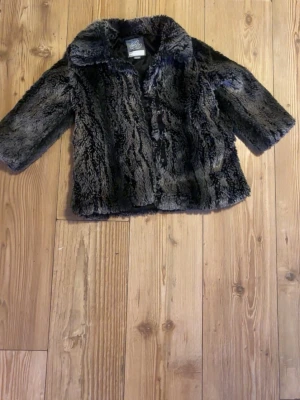 Svart pälsjacka från Lindex - Mysig svart pälsjacka från Lindex med fluffig känsla och tryckknappar framtill. Jackan har en bred krage och är fodrad med svart tyg på insidan. Perfekt för dig som vill ha en statementjacka med cool look.