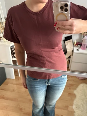 Brun/röd tight t-shirt i bomull - Säljer en enkel brun t-shirt med tight figursydd passform och korta ärmar. T-shirten har en rak söm framtill som detalj och är gjord i mjuk bomull med ett lite tjockare och lyxigt tyg. Perfekt till jeans eller kjol för en clean och stilren look. ☺️☺️ Använd endast en gång.