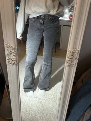 Bootcut jeans från Gina Tricot - Säljer ett par grå bootcut jeans från Gina Tricot i storlek 34. De har mid waist, klassisk femficksdesign och dragkedja med knapp. Materialet är jeans med en snygg tvättad look och passformen är normal. Inte mkt använd, säljer för dom sitter inte 100 på mig.