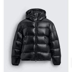 Svart pufferjacka från Zara - Pufferjacka från Zara med huva. Jackan har dragkedja framtill, två fickor med dragkedja. Perfekt för kalla dagar under vintern. Helt ny aldrig använd, köpte fel storlek därav säljer jag den. Storlek L.