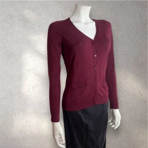 kofta med v-ringning från Stockh LM - Snygg vinröd kofta från Stockh LM med v-ringad hals, långa ärmar och knappar framtill. Koftan har två små fickor och ett diskret broderat på bröstet. #kofta #tröja #stochkLM