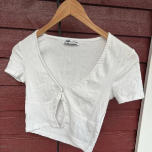 Vit croppad topp med hjärtmönster FB Sister - Supersöt vit croppad topp från FB Sister med små hjärtan som mönster. Toppen har korta ärmar, v-ringning och en snygg knappdetalj framtill med öppning under. Perfekt för dig som gillar gulliga detaljer och en fräsch look.