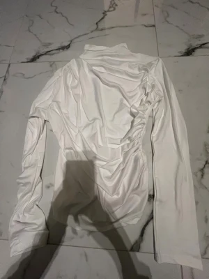 Vit fin långärmad tröja från Emery Rose - Säljer en vit långärmad topp från Emery Rose. Toppen har en snygg rynkad detalj på ena sidan och är tillverkad i ett mjukt, stretchigt material som känns skönt mot huden. Perfekt för dig som gillar stilrena och trendiga plagg med en twist.   (Topen är mindre i storleken)