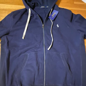 Marinblå hoodie från Polo Ralph Lauren - Snygg marinblå hoodie från Polo Ralph Lauren med vit broderad logga på bröstet. Passar någon som är mellan 182-187cm lång. Priset kan diskuteras.