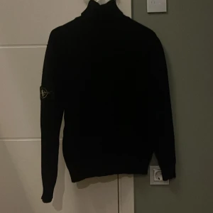 Svart polotröja från Stone Island - Svart polotröja från Stone Island i stickad ull. Klassisk design med ribbade muddar och ikonisk Stone Island patch på vänster ärm. Perfekt för dig som gillar stilrena och exklusiva plagg. Polokrage och långärmad modell. pris kan diskuteras