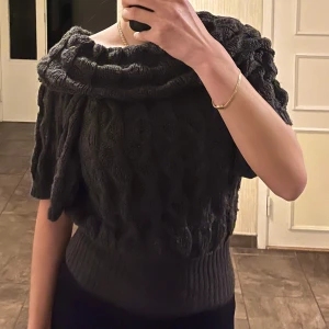 Mörkgrå stickad offshoulder tröja - Mörkgrå stickad tröja med bred offshoulder-krage och korta ärmar. Tröjan har ett snyggt kabelstickat mönster och bred ribbad kant nedtill som ger en schysst passform. Storlek S, normal i storleken. 