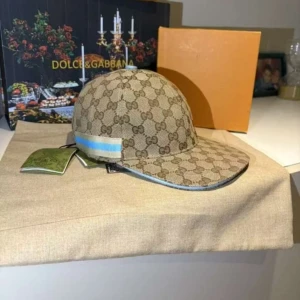 Gucci keps med monogram och blå detalj - Snygg keps från Gucci med klassiskt GG-monogram i beige och brunt. Kepsen har en blå och vit randig detalj på sidan och böjd skärm. Perfekt accessoar för att lyfta din outfit med lyxig känsla. Box finns med och tags