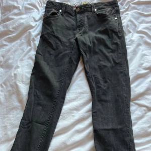 Svarta jeans från Tramarossa - Snygga svarta jeans från Tramarossa med raka ben och klassisk femficksdesign. Jeansen har silverfärgade nitar och en liten metalllogga vid bakfickan. Materialet är mjukt denim och midjan är normal. Perfekta för dig som gillar stilrena och coola jeans.