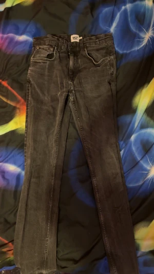 Svarta jeansbyxor med smal passform - Snygga svarta jeansbyxor från 157 med klassisk femficksdesign och smal passform. Jeansen har en mörk tvätt med lätt slitning och raka ben. Perfekt för dig som gillar en stilren look med edge. Byxor är i bra skick och finns inga skador Priset kan absolut diskuteras vid snabb affär.