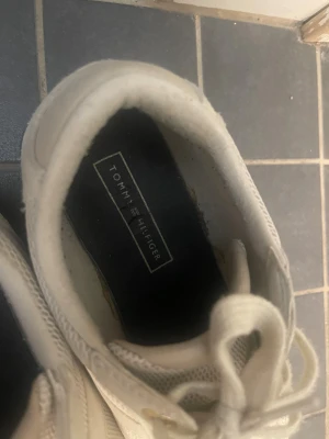 Vita sneakers Tommy Hilfiger pastell - Snygga vita sneakers från Tommy Hilfiger med mesh och mockadetaljer. Skorna har snörning och coola pastellfärgade ränder i rosa, blått och gult på sulan. Klassisk logga bak och diskret branding på sidan. Perfekta för dig som gillar stilrena men ändå unika sneakers.