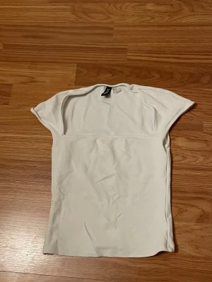 Vit croppad topp från Divided XS - Säljer en vit croppad topp från Divided i storlek XS. Toppen har en fyrkantig halsringning och är kortärmad med en slim passform. Materialet är mjukt och stretchigt, perfekt för att styla med jeans eller kjol. Enkel och clean design utan mönster eller detaljer.