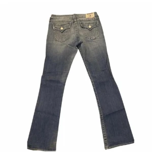 True Religion bootcut jeans blå - Jättefina vintage true religion jeans som jag säljer pga att de inte passar mig. De är bootcut och low waist med ca 83 cm innerbenslängd och midjan är ca 41 cm tvärs över. Har lite slitningar på framsidan av låren som syns på sista bilden och lite slitningar vid sömmen längst ner på benen (skriv för bild) men annars i bra skick. De två första bilderna är från förra säljaren. Skriv för frågor!💗