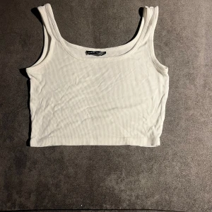 Vit ribbad linnetopp från SHEIN - Säljer en vit croppad linnetopp från SHEIN i storlek XS. Toppen har breda axelband och är ribbad för en snygg textur. Perfekt för varma dagar och enkel att matcha med jeans eller kjol. Materialet är mjukt och stretchigt för skön passform.