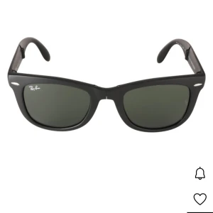 Svarta Ray-Ban Wayfarer solglasögon - Klassiska svarta Ray-Ban Wayfarer solglasögon med rektangulär form och mörka glas. Snygg och tidlös design med Ray-Ban-logga på ena linsen. Kommer med en vit tygpåse för förvaring. Perfekta för att lyfta din stil i solen.