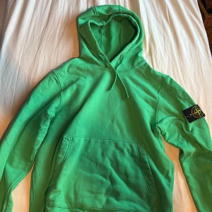 Grön hoodie från Stone Island - Säljer en grön hoodie från Stone Island med klassisk patch på vänster ärm. Tröjan har huva med snörning, stor magficka och ribbade muddar. Materialet är mjuk bomull och modellen är normal passform. Perfekt för dig som gillar streetwear och vill sticka ut. Super fint skicka, inte alls mycket använd.  Strl S, 