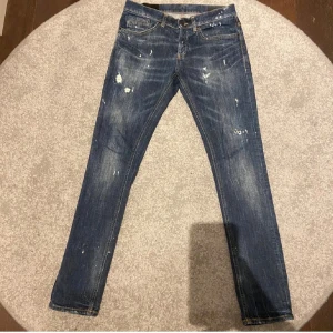 Dondup jeans  - Säljer ett par blå skinny fit jeans från Dondup, tillverkade i Italien. Jeansen har slitna detaljer och diskreta färgstänk för en cool, trendig look. Klassisk femficksmodell med orange sömmar och låg midja. Perfekt för dig som gillar smal passform och streetstil.