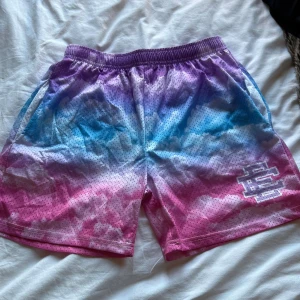 Färgskiftande mesh-shorts från EE - Säljer ett par sjukt snygga mesh-shorts från EE, Made in New York. De har en färgskiftande gradient i lila, blå och rosa med små svarta prickar och elastisk midja. Perfekta för chill eller träning, med två sidofickor och logga på benet.