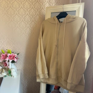 Beige hoodie med dragkedja och huva - Säljer en beige hoodie med dragkedja och huva, perfekt för chill dagar. Modellen är loose fit. Knopprig men går att få bort. I storlek L men jag tar på mig S/M — så funkar perfekt som en ovserzied kofta ☺️