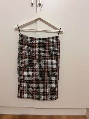 Rutig kjol från Teorema Officewear - Snygg rutig kjol från Teorema Officewear i klassisk pennkjolsmodell. Färgerna är svart, vit, röd och inslag av gul och grön. Kjolen är fodrad och har en strukturerad yta som ger en cool vibe. Perfekt för dig som gillar preppy och stilrena outfits.