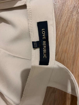 Beige omlottklänning Love Republic - Snygg beige kortklänning från Love Republic med breda axelband och omlottdetalj framtill. Klänningen har en figurnära passform och dragkedja i ryggen. Perfekt för dig som gillar stilrena och eleganta plagg med modern touch.