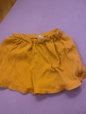 Gula ribbade shorts från Zara - Säljer ett par coola gula shorts från Zara i storlek 140. De har en ribbad struktur och elastisk midja för skön passform. Perfekta för varma dagar och har en loose fit som ger en avslappnad vibe. Materialet känns mjukt och luftigt mot huden.
