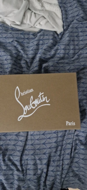Svarta sneakers från Christian Louboutin - (Dem är helt nya och oanvända)Säljer ett par svarta sneakers från Christian Louboutin med ikoniska röda sulor och signaturdetaljer på sidan. Skorna har snörning, rund tå och är tillverkade i mocka med inslag av skinn. Snygg och stilren design som sticker ut med den röda undersidan.
