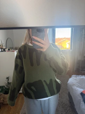 Grön stickad tröja med camouflage - Säljer en grön stickad tröja med coolt camouflage-mönster i mörkare gröna toner. Tröjan har en loose passform och långa ärmar, perfekt för dig som gillar streetstyle och vill ha något bekvämt och snyggt. Passar till både jeans och mjukisbyxor.