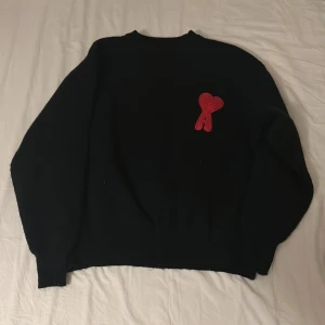 Svart stickad tröja från Ami - Svart stickad tröja från Ami Alexandre Mattiussi med lång ärm och rund hals. På bröstet sitter Ami:s ikoniska röda hjärtdetalj. Tröjan har en clean och chill vibe, perfekt för dig som gillar stilrena plagg med en twist. Jag har andvände den 2 gånger men den är lite för stor på mig