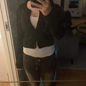 Svart kofta med knappar - Svart, klassisk kofta med rund hals och knäppning framtill. Modellen är lite croppad och har långa ärmar. Perfekt att slänga över en topp eller linne. Mjuk och skön, passar dig som gillar enkel och stilren look.