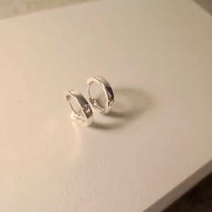 Mindre chunky silvriga hoops örhängen - Säljer ett par chunky hoops i blankt silverfärgat material. De är runda och har en stilren, minimalistisk design som passar perfekt för dig som gillar enkla men snygga smycken. Lätta att matcha med andra accessoarer och har ett klassiskt klicklås.