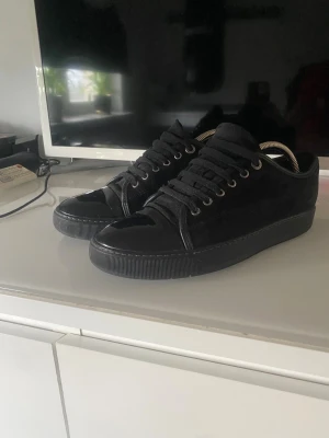 Lanvin svart - Säljer ett par svarta sneakers med snygg lackad tå och snörning. Skorna har en rund tå och platt sula, med ovandel i mocka och detaljer i blankt syntetmaterial. Perfekt för dig som gillar stilrena och moderna skor med lite edge. Vid snabb affär går det att diskutera priset‼️‼️