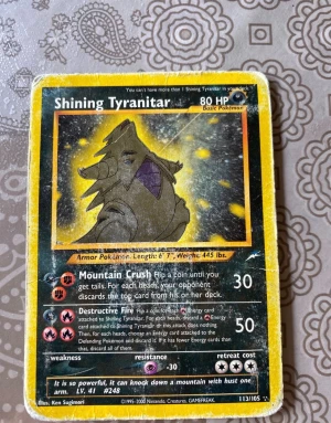 Shining Tyranitar - Sällsynt Pokémonkort med cool Tyranitar-illustration och unika attacker som Mountain Crush och Destructive Fire. Perfekt för samlare och Pokémon-fans som vill ha något extra i sin kortlek. Kortet har tydliga tecken på användning men är fortfarande en grym retropryl!