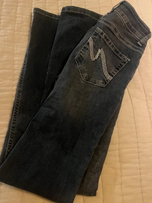Blå low jeans  minsta storleken Nelly 32 - Snygga blå jeans från Nelly med bootcut passform och klassisk femficksdesign. Jeansen har en cool detalj med vit broderad söm på bakfickan och dubbla metallknappar i midjan. Materialet är jeans med en mörk tvätt och kontrastsömmar. OBS!!! BARA VID SERISÖA (BESTÄMDA) KÖP!!!!!