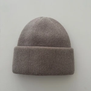 Beige ribbad mössa i ull - Snygg beige mössa med bred uppvikt kant och ribbad struktur. Tillverkad i mjuk ull som håller dig varm och ger en chill vibe. Perfekt för kalla dagar och enkel att matcha med din jacka eller hoodie.