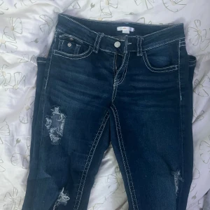 Mörkblå bootcut jeans med slitningar - Snygga mörkblå jeans med tydliga slitningar och hål på benen. Bootcut-modell med kontrasterande vita sömmar. De är från Ginatricot Young i Storlek 164