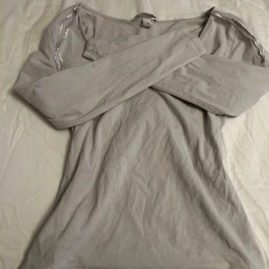 Vit långärmad tröja  - Snygg basic vit långärmad tröja från H&M med diskreta silverdetaljer längs axlarna. Tröjan har en enkel och clean design med rund hals och är tillverkad i mjuk bomull som är skön mot huden. Perfekt för dig som gillar stilrena plagg med en twist.