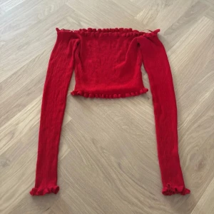 Röd ribbad offshoulder topp FB Sister - Säljer en röd ribbad offshoulder topp från FB Sister i storlek XS. Toppen har långa ärmar och volangdetaljer vid halsringning, ärmslut och nederkant. Materialet är mjukt och stretchigt, perfekt för dig som gillar trendiga och färgstarka plagg.