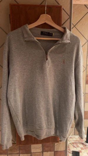 Grå half zip tröja Polo Ralph Lauren - Grå långärmad tröja från Polo Ralph Lauren med half zip och klassisk krage. Tröjan har broderad logga på bröstet och är tillverkad i mjuk bomull. Perfekt för chill dagar och snygg att matcha med jeans