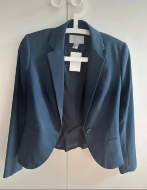 Mörkblå kavaj från H&M  - Snygg mörkblå kavaj från H&M med klassisk krage och en knapp framtill. Figursydd modell pi och fodrad i matchande blått tyg. Perfekt för dig som gillar stilrena och enkla plagg